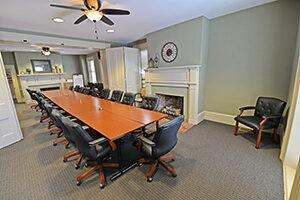 View of the Cochran House conference room. Light green walls, cream trim, two fireplaces, and a long executive style conference table with black leather chairs.