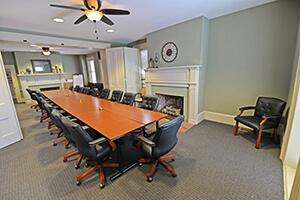 View of the Cochran House conference room. Light green walls, cream trim, two fireplaces, and a long executive style conference table with black leather chairs.