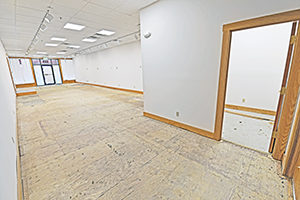 Uptown Plaza, Suite 115, view 3, back to front, white walls, bright lighting, elongated space, unfinished floor, glimpse of the enclosed space.