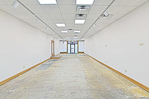 Uptown Plaza, Suite 115, view 3, back to front, white walls, bright lighting, elongated space, unfinished floor.