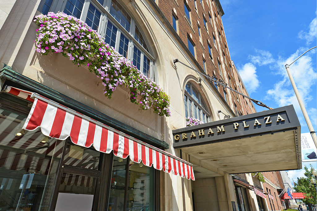 Close up of Graham Plaza marquee sign, red and white candy stripe awning, and a large arched window with cascading purple and magenta flowers.